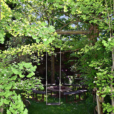 Ein Garten mit Schaukel, Sitzgelegenheiten und viel Grün.