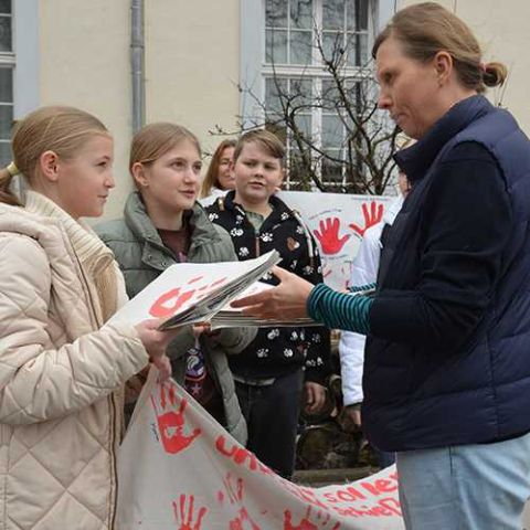 Zwei Schülerinnen überreichen der Bundestagsabgeordneten Corinna Rüffer rote Handabdrücke als Zeichen des Protests gegen Kindersoldaten.