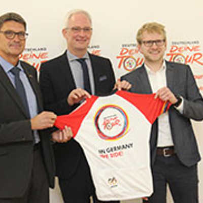 OB Wolfram Leibe (Mitte) und Landrat Günther Schartz (l.) präsentieren mit Matthias Pietsch, Projektmanager des Veranstalters ASO (r.), das offizielle Trikot der Deutschland-Tour 2018.