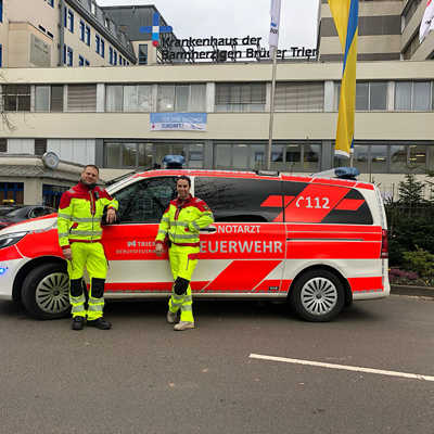 Mitarbeitende des Rettungsdienstes der Trierer Feuerwehr präsentieren die neue neongelbe Einsatzkleidung vor einem Notarzteinsatzfahrzeug. Foto: Feuerwehr Trier