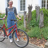 Eine Fau steht neben einem roten Fahrrad und hält es fest