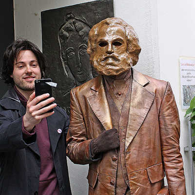 Der junge Karl Marx (Tobias Schwieger) macht vor dem Wohnhaus seiner damaligen Freundin Jenny ein Selfie mit seinem Bronze-Alter-Ego und der Gedenkplakette für Jenny von Westphalen.