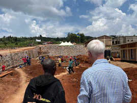 OB Wolfram Leibe und ein Mann aus Ruanda sind von hinten zu sehen. Sie blicken auf eine Baustelle, auf der gerade die Grundmauern eines neuen Schulgebäudes errichtet werden.