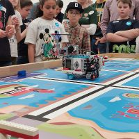 Kinder stehen rund um einen Wettbewerbstisch und schauen einem Roboter zu