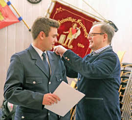 Dezernent Ralf Britten (r.) befördert Luca Linz zum Feuerwehrmann und heftet ihm die Schulterklappen an.