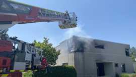 Das Bild zeigt das brennende Haus in Olewig. Von links ragt eine Drehleiter der Feuerwehr ins Bild.