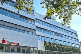 Ein mehrstöckiges Bürogebäude mit Fensterreihen, Fassadenbegrünung und Logo der Sparkasse
