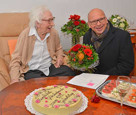 Katharina Pallien ist an ihrem 100. Geburtstag gut aufgelegt und witzelt mit Ortsvorsteher Dominik Heinrich, der ihr Blumen und OB-Wein schenkt.