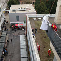 Ein Feuerwehrmann im Engelskostüm wird von Höhenretterrn in roter Montur in einen Hof abgeseilt