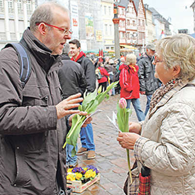 Zum Start der Aktionstage „Wir für Demokratie“ überreicht Thomas Zuche (Caritas) einer Passantin auf dem Hauptmarkt eine Frühlingsblume mit Info-Flyer.