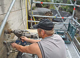Igor Spetz, Mitarbeiter der Erkelenzer Bohrgesellschaft aus Wittlich, treibt  einen Bohrkern in die Stützmauer an der Talseite der Napoleonsbrücke. Zuvor war ein Gerüst in luftiger Höhe montiert worden.