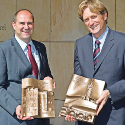 Thomas Egger (links) präsentiert die Stifterplatte mit Dreikönigenhaus und Frankenturm, Jan Niewodniczanski die zweite Plakette mit Römerbrücke und Mariensäule. Foto: Agenturhaus