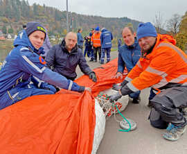Julian Lehnart, Alexander Hammel und Michael Eiden erläutern Dr. Thilo Becker die Funktionsweise des orangefarbenen, schlauchartigen Mobildeichs.