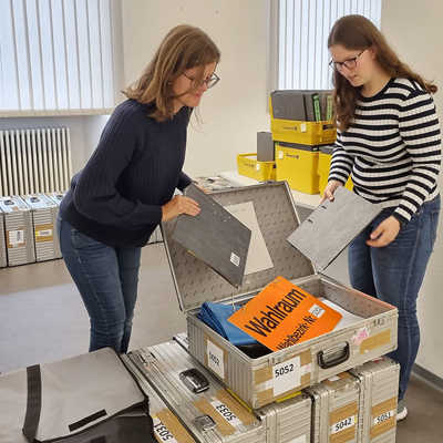 Kristina Reis und Antonia Willger vom Wahlbüro (v. l.) packen zwei Ordner für das Wählerverzeichnis sowie ergänzende Unterlagen in den Koffer für eines der 66 Wahllokale im Stadtgebiet.