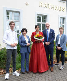 Melika Zare steht in einem roten Kleid und mit einem Sonnenblumenstrauß vor dem Rathaus neben Felix von Nell, Zoleykha Zare, Wolfram Leibe und Christine Becker.