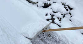 Das Bild zeigt eine Schneeschaufekl im Einsatz auf einem tief verschneiten Gehweg.