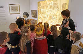 Kuratorin Dorothée Henschel führt kostümierte Kinder der Grundschule am Dom durch die Karnevals-Ausstellung.