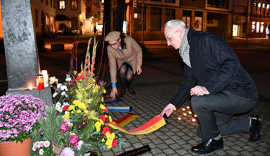 OB Wolfram Leibe und die Vorsitzende der Jüdischen Kultusgemeinde, Jeanne Bakal, knien mit einem Blumengesteck auf dem Boden.