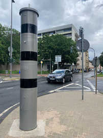 An der Straßenkreuzung von Kaiserstraße und Hindenburgstraße steht eine hohe Säule, der Ampelblitzer. Im Hintergrund fahren Autos vorbei.