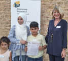 Mazen Mabrouke präsentiert mit seiner Familie die Diesterweg-Urkunde, die ihm Sabine Plate-Batz (Nikolaus-Koch-Stiftung) überreicht hatte.
