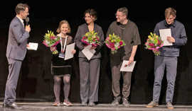 Die vier Preisträger stehen nebeneinander, jeweils mit einem Blumenstrauß in der Hand, links davon der Moderator