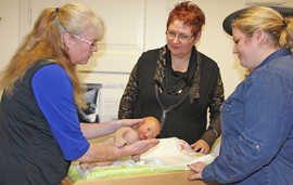 Hebamme Ute Bösen (links) erläutert wie werdende Eltern mit einer Puppe Tipps für die Pflege und medizinische Versorgung des Säuglings erhalten. 