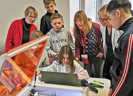 Schülerinnen und Schüler zeigen Bildungsministerin Stefanie Hubig (2. v. r.) und Birgit Pikowsky, Direktorin des Pädagogischen Landesinstituts (links), wie man mit dem Lasercutter graviert, 3D-Modelle druckt oder einen eigenen Sticker erstellt. Foto: Medienanstalt Rheinland-Pfalz