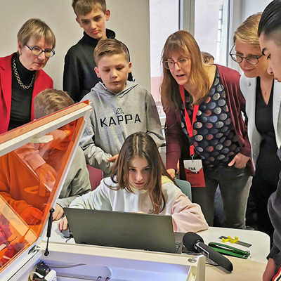 Schülerinnen und Schüler zeigen Bildungsministerin Stefanie Hubig (2. v. r.) und Birgit Pikowsky, Direktorin des Pädagogischen Landesinstituts (links), wie man mit dem Lasercutter graviert, 3D-Modelle druckt oder einen eigenen Sticker erstellt. Foto: Medienanstalt Rheinland-Pfalz