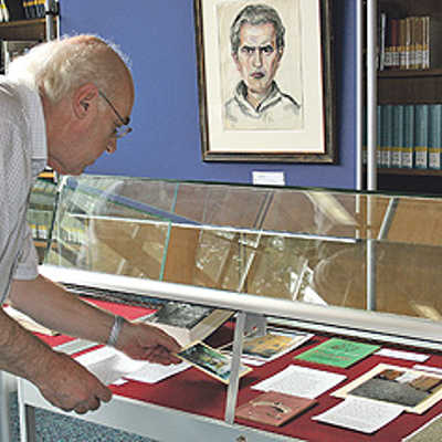 Kurator Günther Nicolin (Stefan-Andres-Gesellschaft Schweich) arrangiert in einer Vitrine die letzten Exponate. Im Hintergrund ein Selbstporträt des Schriftstellers aus dem Jahr 1940.