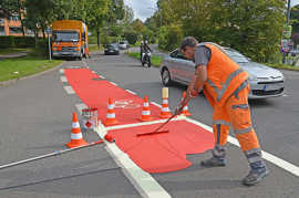 Ein Mitarbeiter der Firma Meiser Fahrbahnmarkierung aus Quierscheid verteilt frische Farbe über eine Radverkehrsfurt in der Hans-Böckler-Allee.