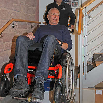 Andreas Rump, Vorsitzender des Seniorenbüro-Vereins, wird von Jürgen Wingertszahn in einem Rollstuhl mit dem darunter montierten Steiger in den ersten Stock befördert. Für den Einsatz des Geräts, dessen Akku für 180 bis 200 Stufen reicht, ist eine Bedienperson nötig. 