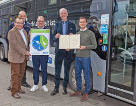 Elmar Kandels, Thomas Hüser und Arndt Müller (SWT) stehen vor einem Elektrobus und präsentieren zusammen mit OB Wolfram Leibe und dessen Büroleiter David Natus die Förderurkunde und ein Werbemotiv für die E-Bus-Flotte.