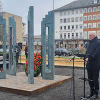 OB Wolfram Leibe steht neben der Gedenkskulptur an einem Rednerpult mit Mikrofon