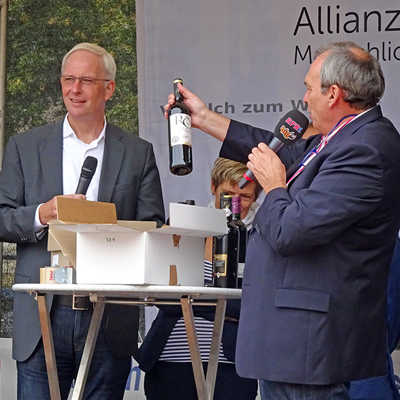 OB Wolfram Leibe, DRK-Vorstandsvorsitzende Anke Marzi (verdeckt) und Auktionator Thomas Vatheuer (v. l.) bringen Spitzenweine für den guten Zweck unter das Volk.