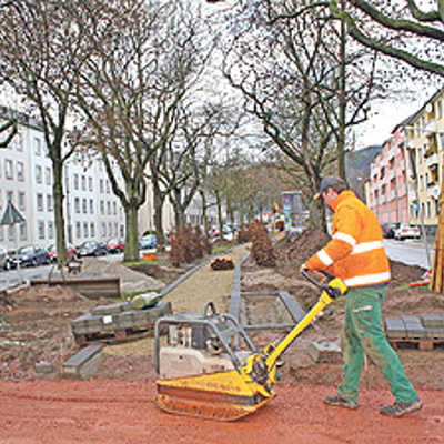 Bauarbeiter Manfred Müller befestigt mit einer Rüttelplatte eine Fläche in der Nähe des Trafohäuschens, Dort wird Pflaster verlegt. Dahinter ist der neu angelegte Weg Richtung Moselufer erkennbar.