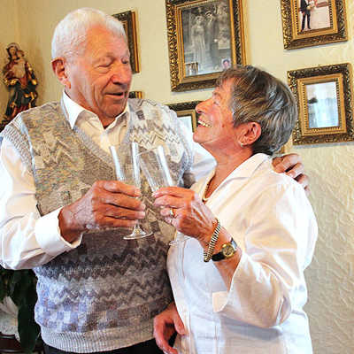 Zum Start der Feierlichkeiten rund um ihre Eiserne Hochzeit stoßen Irmi und Rudi Kugel vor der Wand mit den Familienfotos mit einem Glas Sekt an.