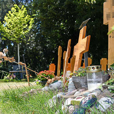 Bei einer Urnengemeinschaftsanlage werden nach dem Entfernen der zunächst nach der Bestattung aufgestellten Holzkreuze Plaketten mit den Namen der Verstorbenen an einer gemeinsamen Stele (hinten Mitte) angebracht. 