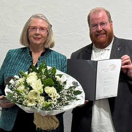 Gabriele Lohberg hält einen Blumenstrauß, Markus Nöhl überreicht ihr eine Urkunde.
