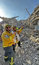 Zwei Katastrophenhelfer stehen in einem Trümmerfeld eingestürzter Häuser