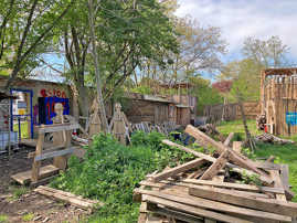 Balekn, Werkstücke und Hütten aus Holz stehen in einem Garten.