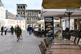 Terrassen von Gaststätten mit Stühlen, Tischen und Sonnenschirmen in der Simeonstraße mit Blick zur Porta Nigra. 