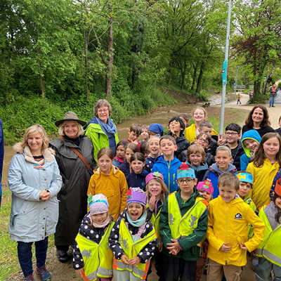 Baudezernent Dr. Thilo Becker, Ministerin Katrin Eder und Olewigs Ortsvorsteherin Petra Block (v. l.) freuen sich mit Kindern der Grundschule und der Kita Olewig über den renaturierten Bach. Die Kinder umrahmten die Veranstaltung musikalisch und erklärten einzelne Schritte der Renaturierung.