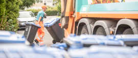 Ein Müllwerker rollt zwei Abfalltonnen zum Sammelfahrzeug