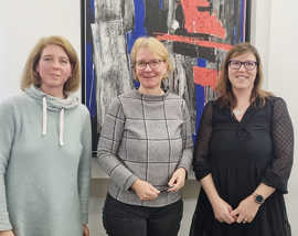 Drei Frauen stehen nebeneinander vor einem bunten Gemälde