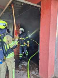 Drei Feuerwehrleute sind im Einsatz zu sehen. Einer hält ein Garagentor geöffnet, zwei kommen unter Atemschutz mit Taschenlampe aus dem Raum.