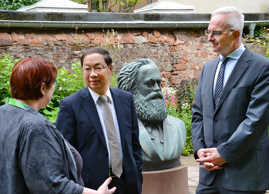 Elisabeth Neu, die kommissarische Leiterin des Museums Karl-Marx-Haus, erläutert Shi Mingde und Wolfram Leibe die Kunst im Garten des Geburtshauses.