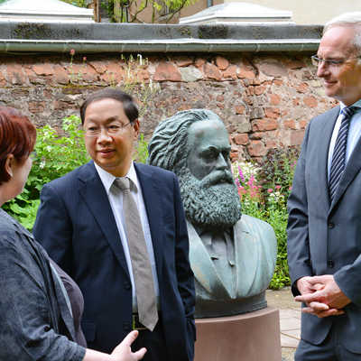 Elisabeth Neu, die kommissarische Leiterin des Museums Karl-Marx-Haus, erläutert dem chinesischen Botschafter Shi Mingde und OB Wolfram Leibe die Kunst im Garten des Geburtshauses.