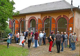 Beim Einweihungsfest stehen viele Menschen an Stehtischen vor der geöffneten Orangerie in Kürenz und unterhalten sich.