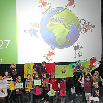 Gemeinsam mit Bürgermeisterin Angelika Birk (hinten Mitte) und Julia Koch (ADD, hinten links), präsentieren die Kinder ihre gebastelten Plakate, auf denen steht, wieviele Meilen sie gesammelt haben. 