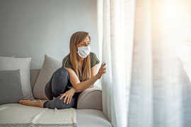 Eine Frau sitzt mit Schutzmaske allein in ihrer Wohnung